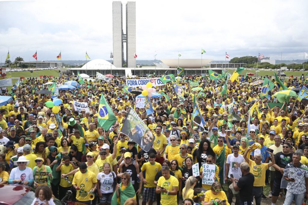 Manifestantes pró-Bolsonaro vestem camisas verde e amarelo e empunham bandeiras do Brasil e cartazes contra o PT